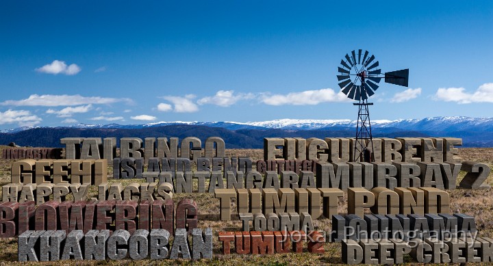 Damn.jpg - Dam(n).  The Snowy Scheme entailed the construction of some 16 dams across the mountains, ranging in size from the huge (Eucumbene, with a capacity of nearly five billion cubic metres) to the tiny (Deep Creek, capacity just five thousand cubic metres). Construction took 20 years, with work on the first dam (Guthega) starting in 1950, and the last (Talbingo) not completed until 1970.They now form a prominent, perhaps dominant, feature of the mountain landscape, especially seen when flying over the region. They fill river valleys that were previously home to remote alpine rivers.  Mountain forests, fine farming country (e.g. where the Blowering Dam now sits), whole towns (‘Old’ Adaminaby and ‘Old’ Jindabyne) have been inundated to achieve the goals of the Scheme. The names of the sixteen dams sit on a hillside looking out to the snow-covered Crackenback and Main Ranges, looking a little like monumental masonry. The windmill suggests alternative technologies for generating power and pumping irrigation water.